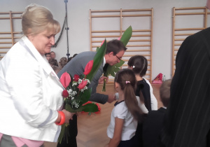 Uczniowie wręczają kwiaty dyrekcji szkoły